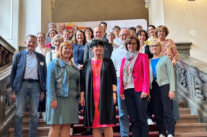Auf einer Treppe steht eine Gruppe Personen. Alle lächeln in Richtung der Kamera.